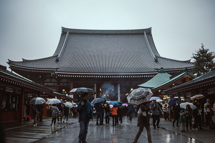 Crowd with umbrellas at Japanese temple in rain
