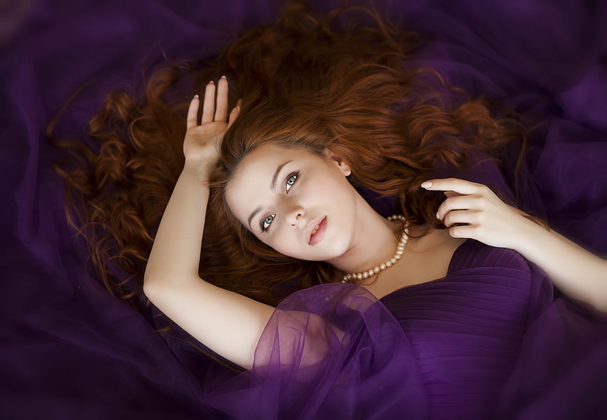 Beautiful woman with red hair lying on purple fabric