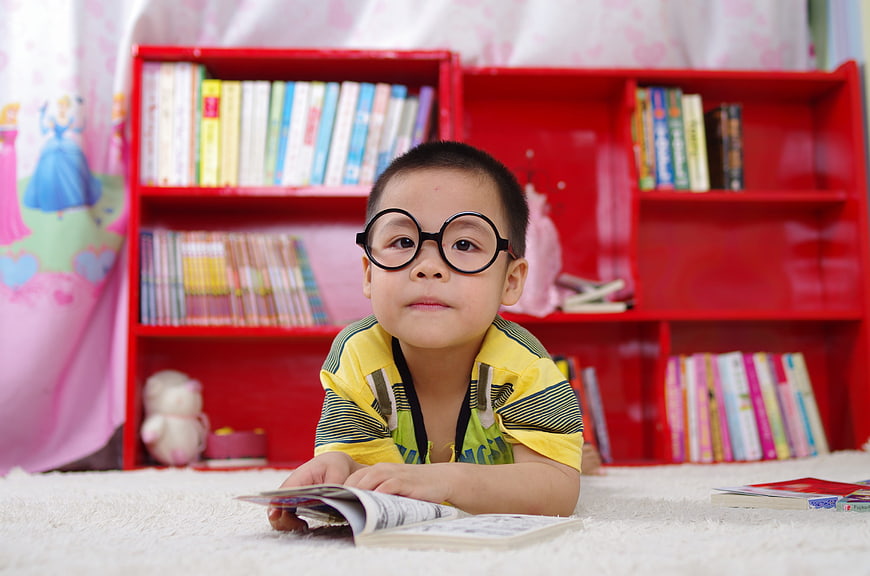 Cute boy with glasses reading book on floor