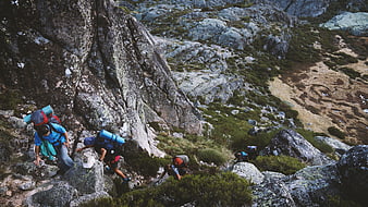 Hikers with backpacks climbing steep rocky mountain trail