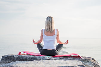 Woman meditating on rock by ocean