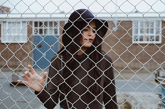 Woman in black hat looking through chain link fence
