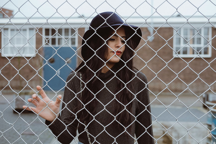 Woman in black hat looking through chain link fence