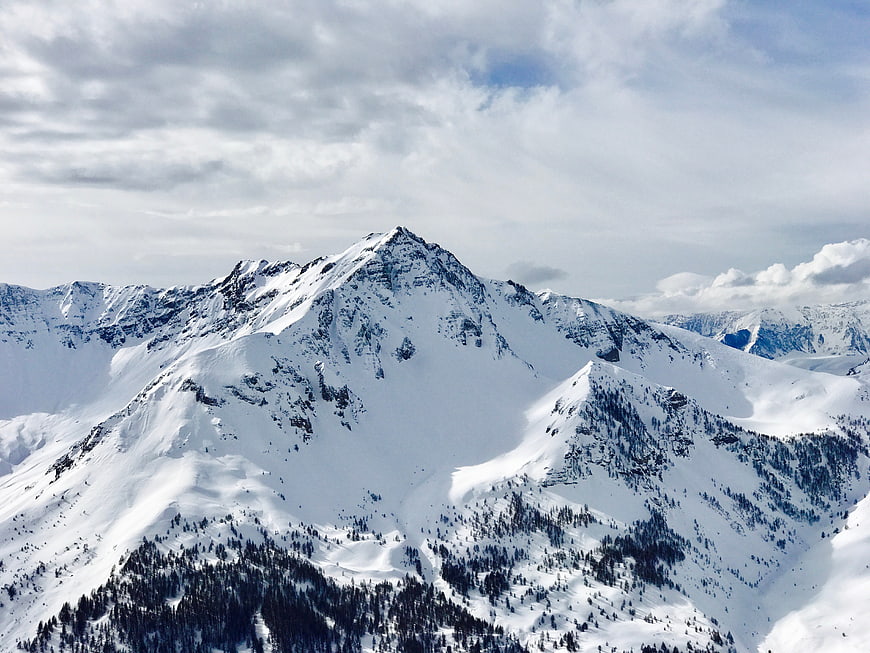 Snowy mountain peak with clouds and pine trees