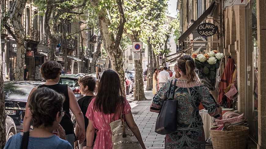 People walking down a sunny tree-lined European street