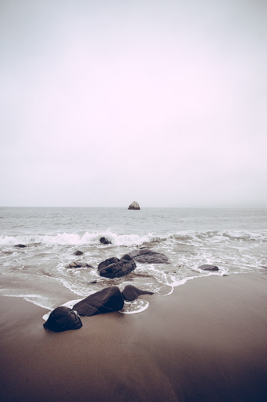 Serene Misty Ocean Beach with Dark Rocks and Waves