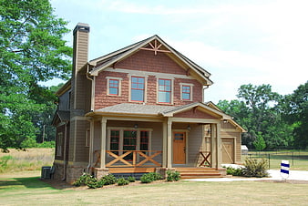 Two-story brown shingle house with front porch and trees