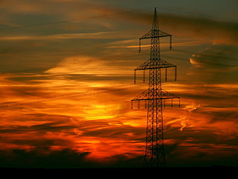 Silhouette of High Voltage Power Line Tower Against Vibrant Orange Sunset Sky