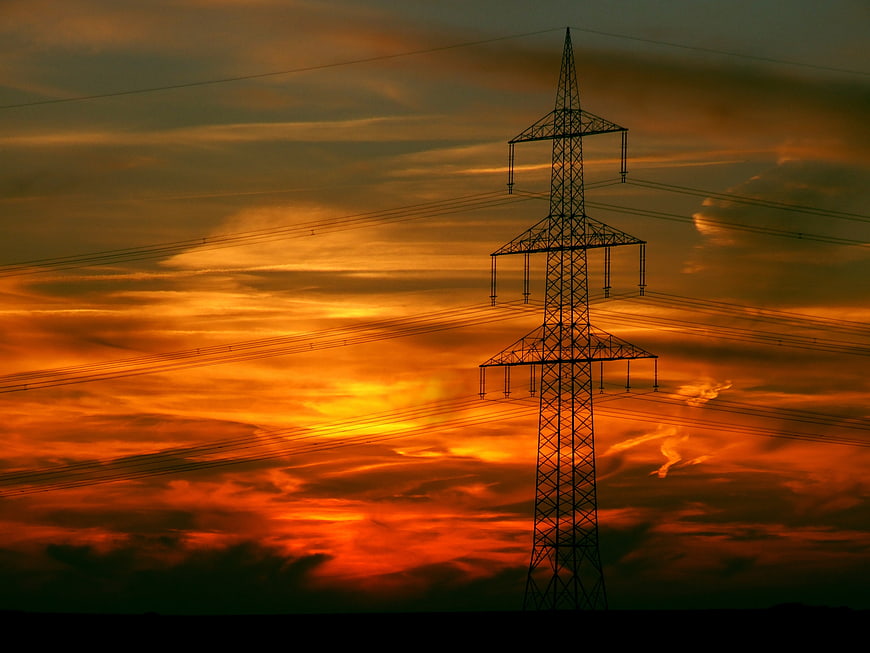 Silhouette of High Voltage Power Line Tower Against Vibrant Orange Sunset Sky