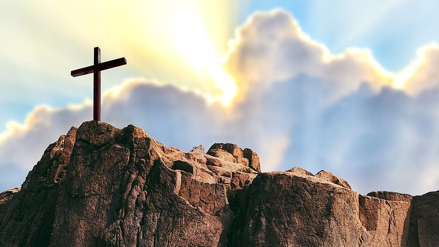 Wooden cross on rocky mountain peak with divine light rays in cloudy sky