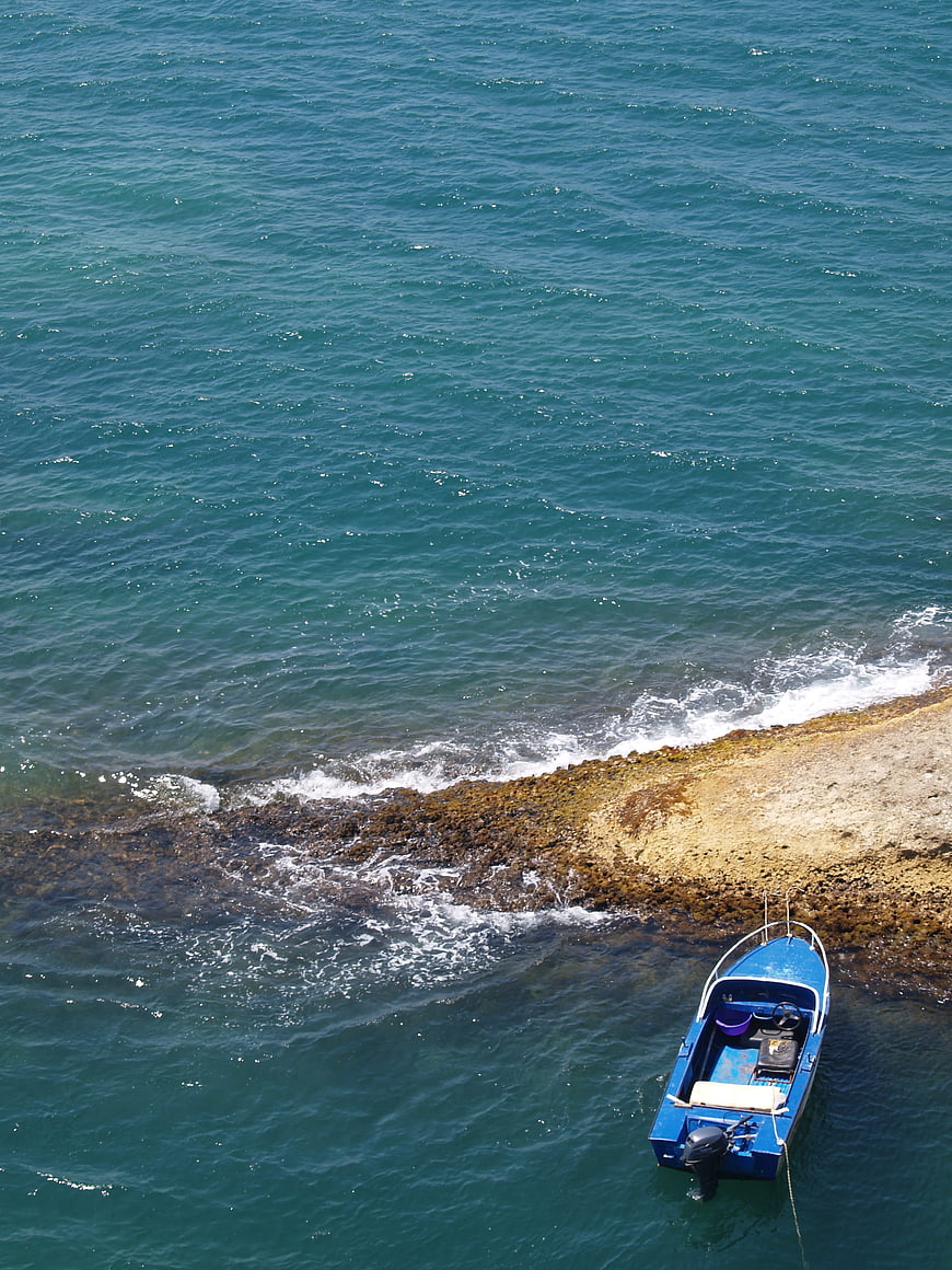 Aerial view of blue motorboat near rocky coastline