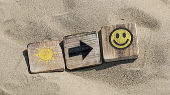 Wooden blocks with sun, arrow, and smiley icons on sand