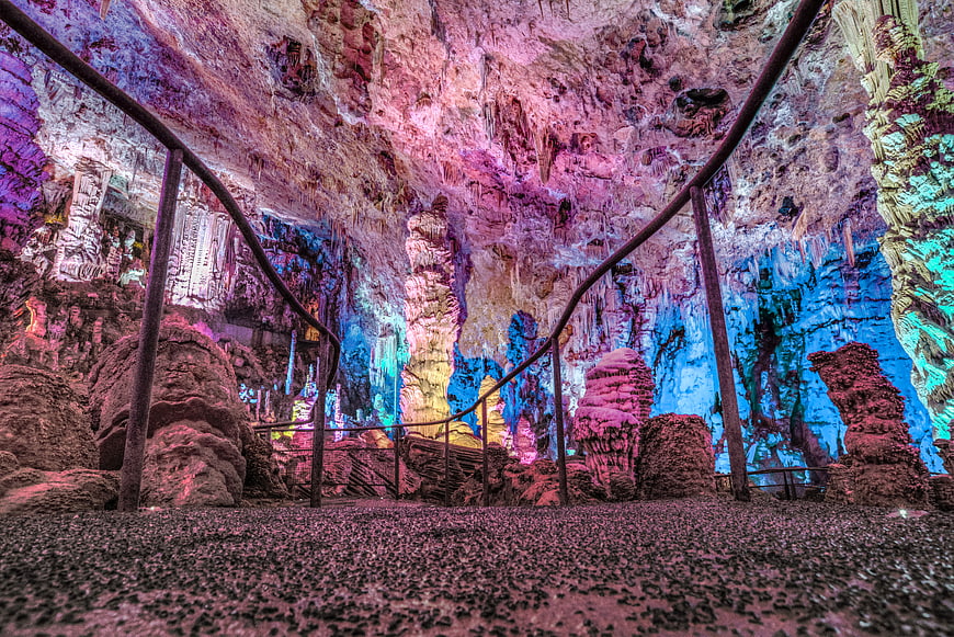 Colorful illuminated cave interior with stalactites and walkway