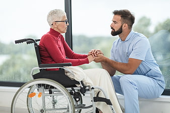 Male nurse holding hands with elderly woman in wheelchair