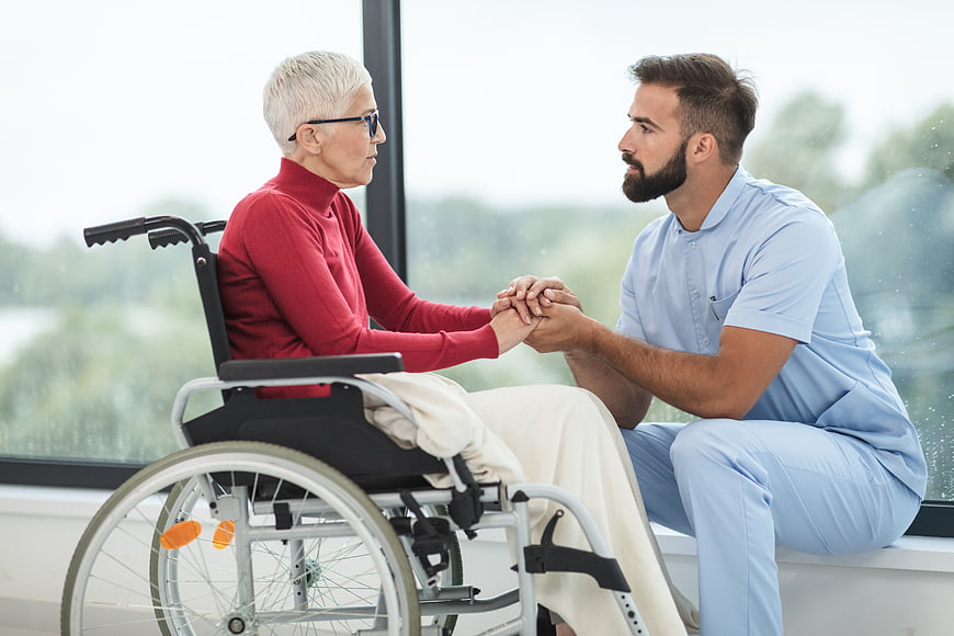 Male nurse holding hands with elderly woman in wheelchair