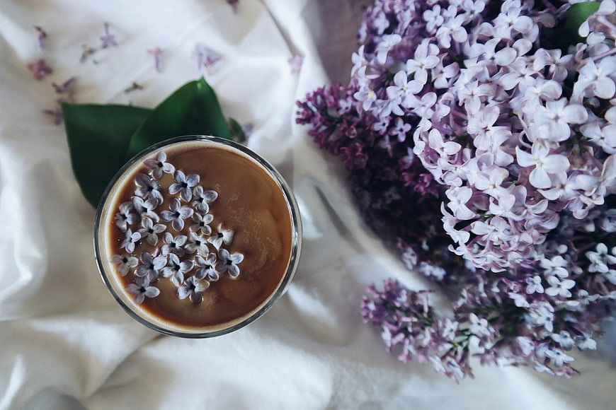 Overhead view of iced coffee with lilac flowers on white linen