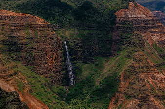 Dramatic waterfall cascading down rugged green and brown mountain cliffs