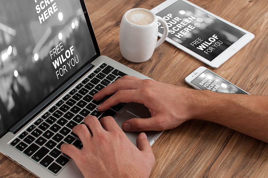 Hands typing on laptop with tablet and smartphone mockup