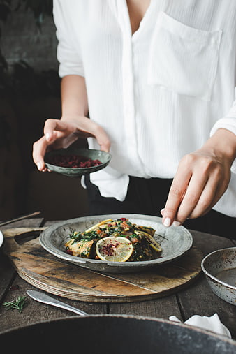 Woman seasoning healthy fish dish with spices