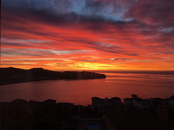 Vibrant red sunset over coastal town and calm ocean
