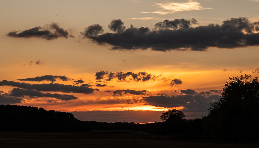 Dramatic sunset over silhouetted landscape with clouds