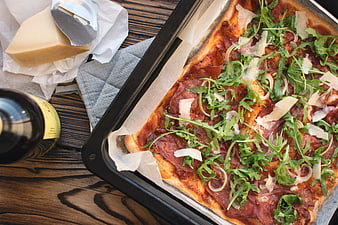 Homemade rectangular pizza with prosciutto and arugula on wooden table