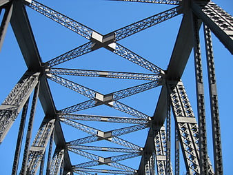 Low angle view of steel bridge truss against blue sky