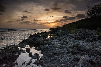 Dramatic Sunset Over Rocky Coastal Shoreline with Clouds
