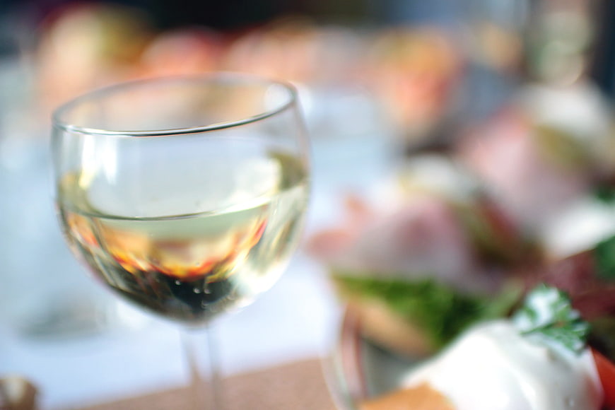 Close-up of white wine glass with blurred appetizers