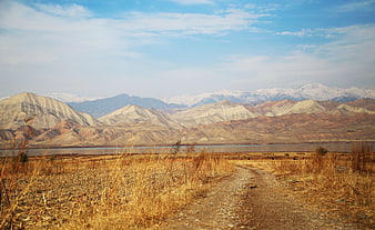 Dirt road leading to lake with snow-capped mountains