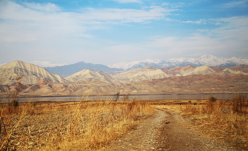 Dirt road leading to lake with snow-capped mountains