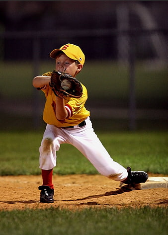Young boy in yellow uniform catching baseball at first base