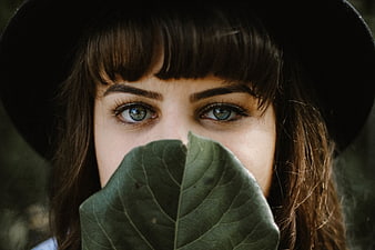 Close-up of woman with blue eyes holding green leaf