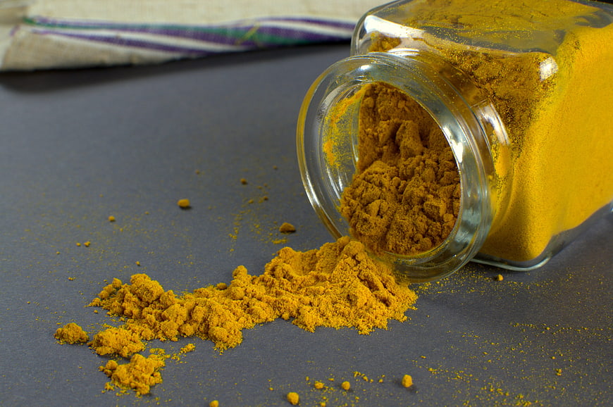 Spilled Turmeric Powder In Glass Jar On Dark Surface