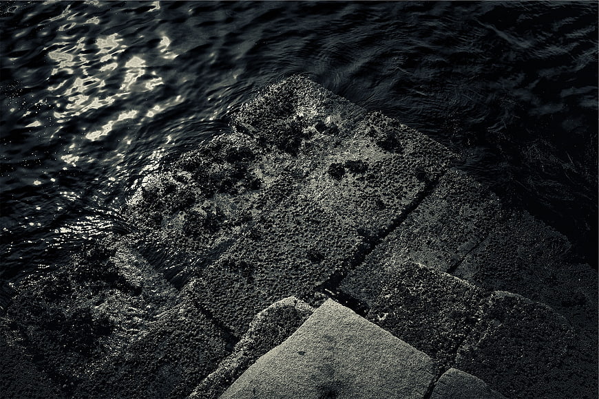 Dark textured concrete steps meeting rippling water at night