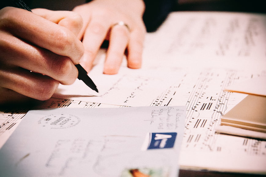Close-up of hands writing on sheet music with postcard