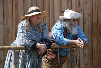Senior couple in vintage western costumes leaning on wooden fence