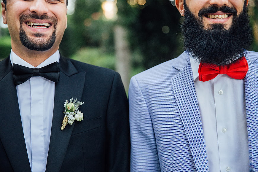 Two smiling groomsmen in suits with bow ties