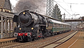 Black steam locomotive pulling green passenger cars at a station