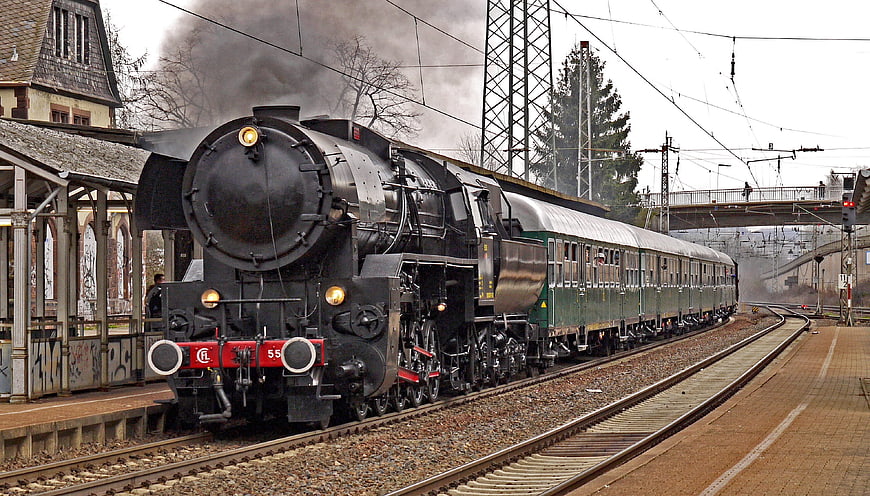 Black steam locomotive pulling green passenger cars at a station