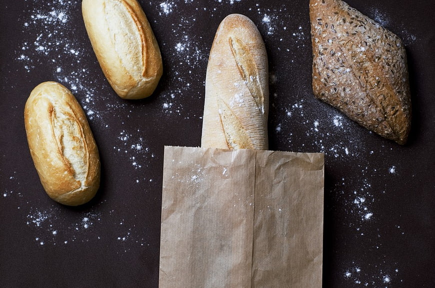 Fresh artisan bread loaves and baguette in paper bag on dark background
