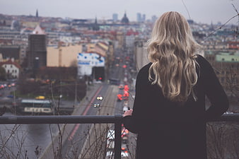 Woman with blonde hair looking at city skyline from bridge