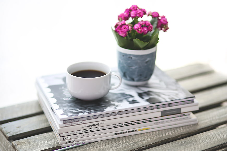 Coffee cup and pink flowers on stack of magazines