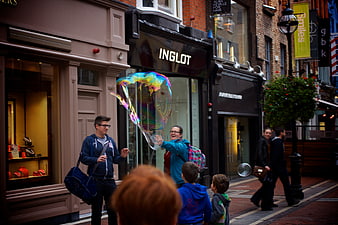 Woman making giant rainbow bubble for children on city street