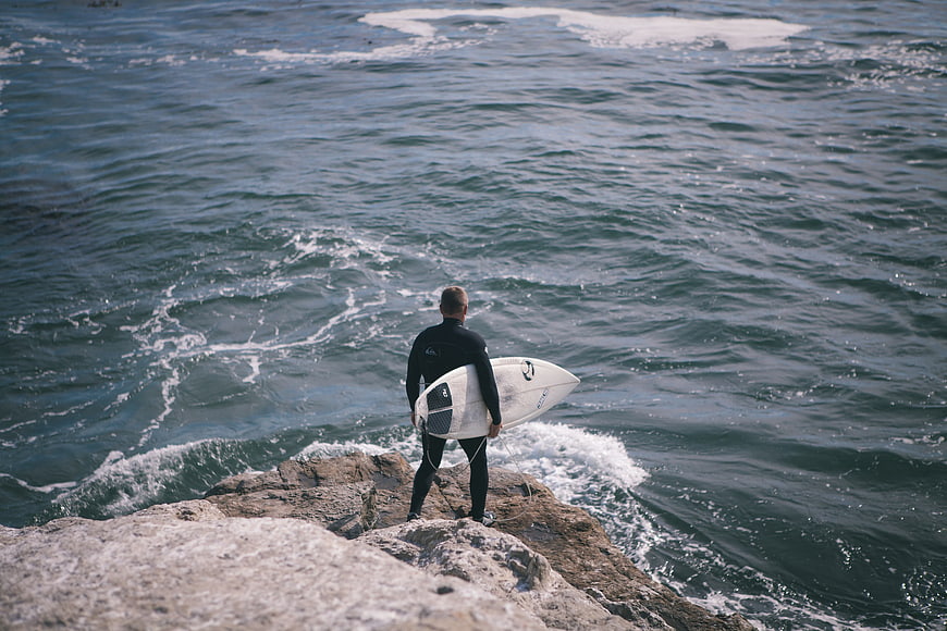 Surfer standing on rocky cliff overlooking ocean waves