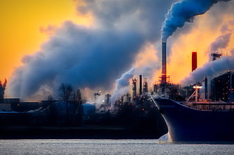 Industrial factory smokestacks emitting pollution at sunset