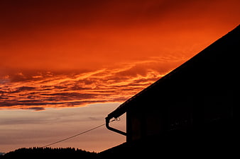 Dramatic orange sunset sky behind dark house silhouette