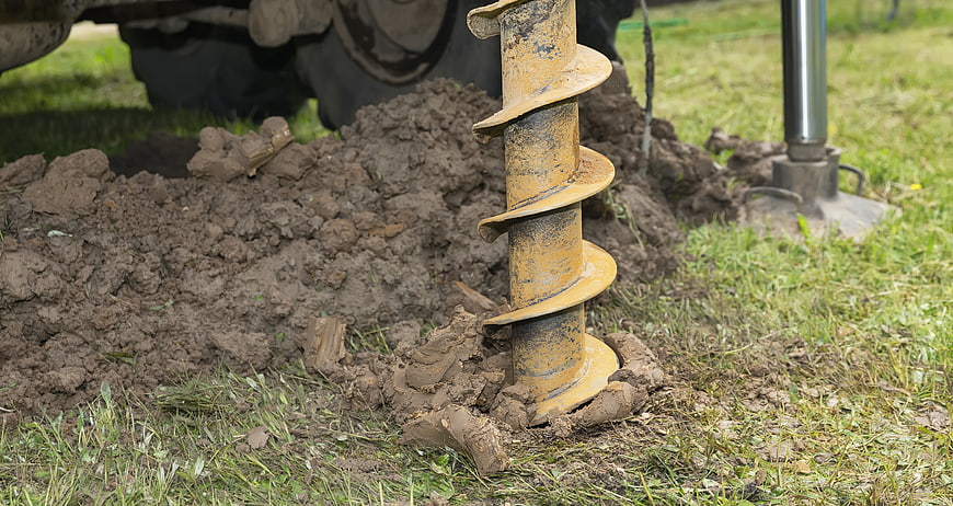 Yellow auger drill bit digging into soil for well drilling