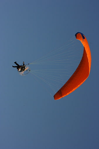 Orange Powered Paraglider Flying Against Blue Sky