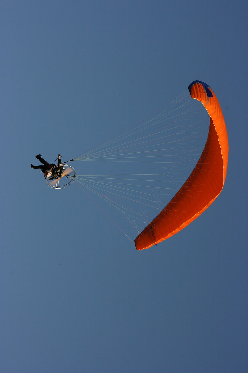 Orange Powered Paraglider Flying Against Blue Sky